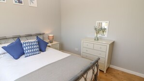 A bedroom with a bed, bedside table, lamp, dresser, mirror, and wall art. - Bankwell Cottage (Newcastle-upon-Tyne)