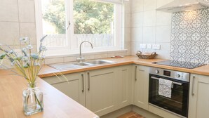 A modern kitchen with a window, a sink, a stove, and light-colored cabinets. - Bankwell Cottage (Newcastle-upon-Tyne)
