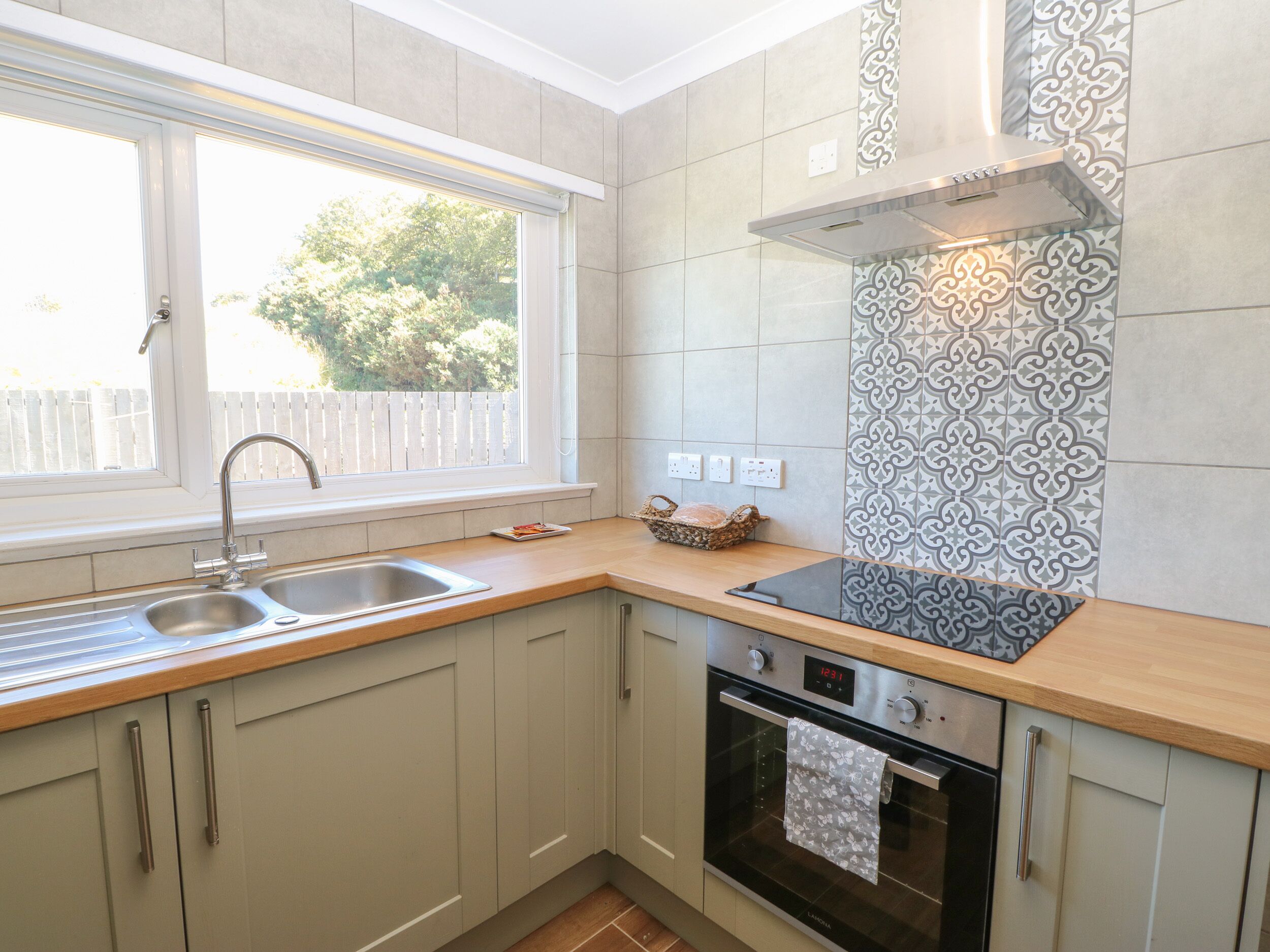 A kitchen with a window, a sink, a stove, and patterned backsplash tiles.