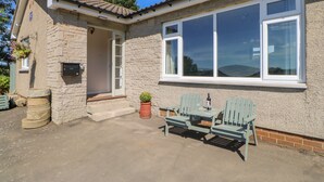 A stone house with a tiled roof, a large window, and a small patio with two green chairs and a table. - Bankwell Cottage (Newcastle-upon-Tyne)