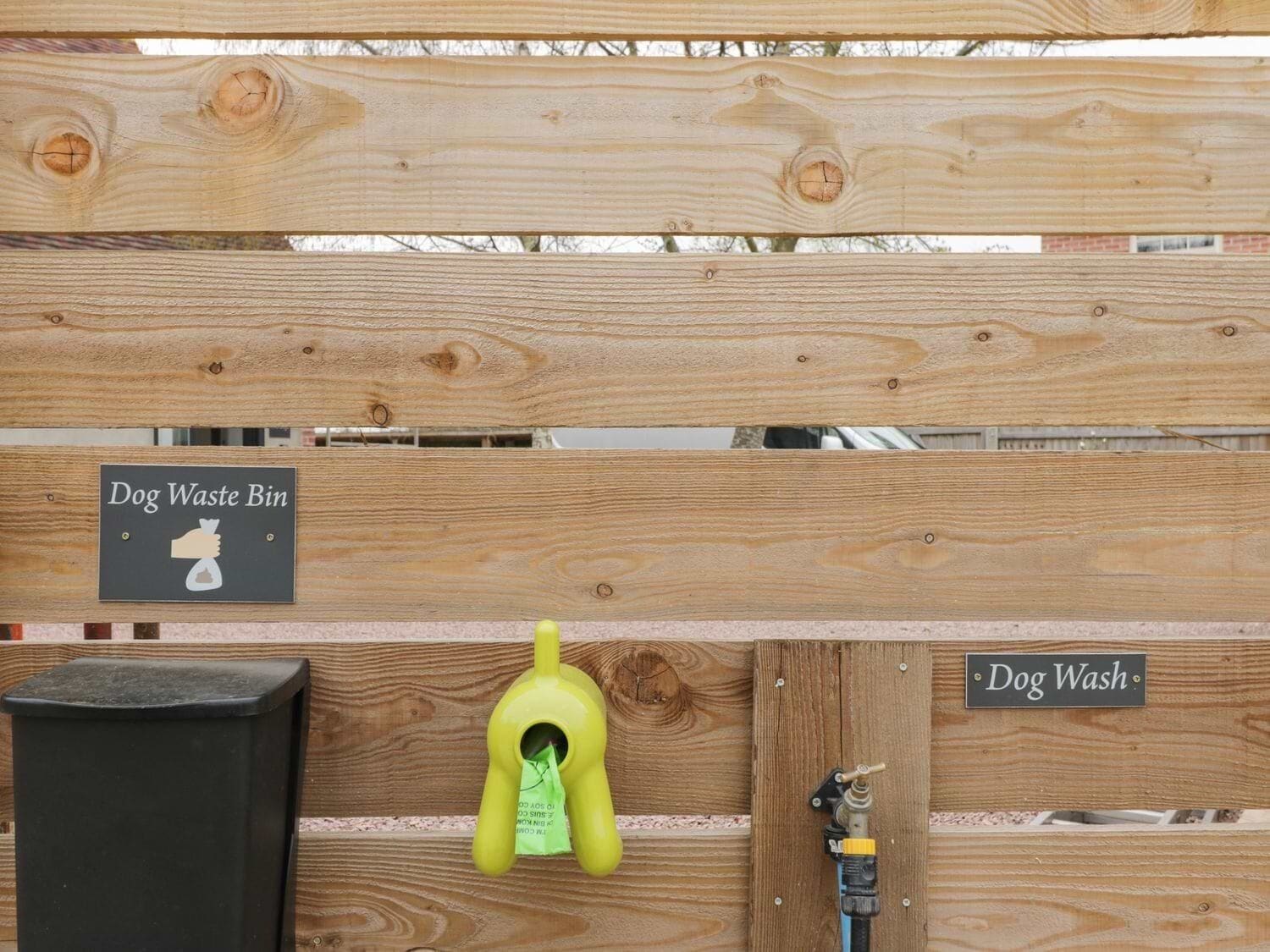 Une clôture en bois, avec une poubelle pour les déjections canines et un espace dédié au lavage des chiens.