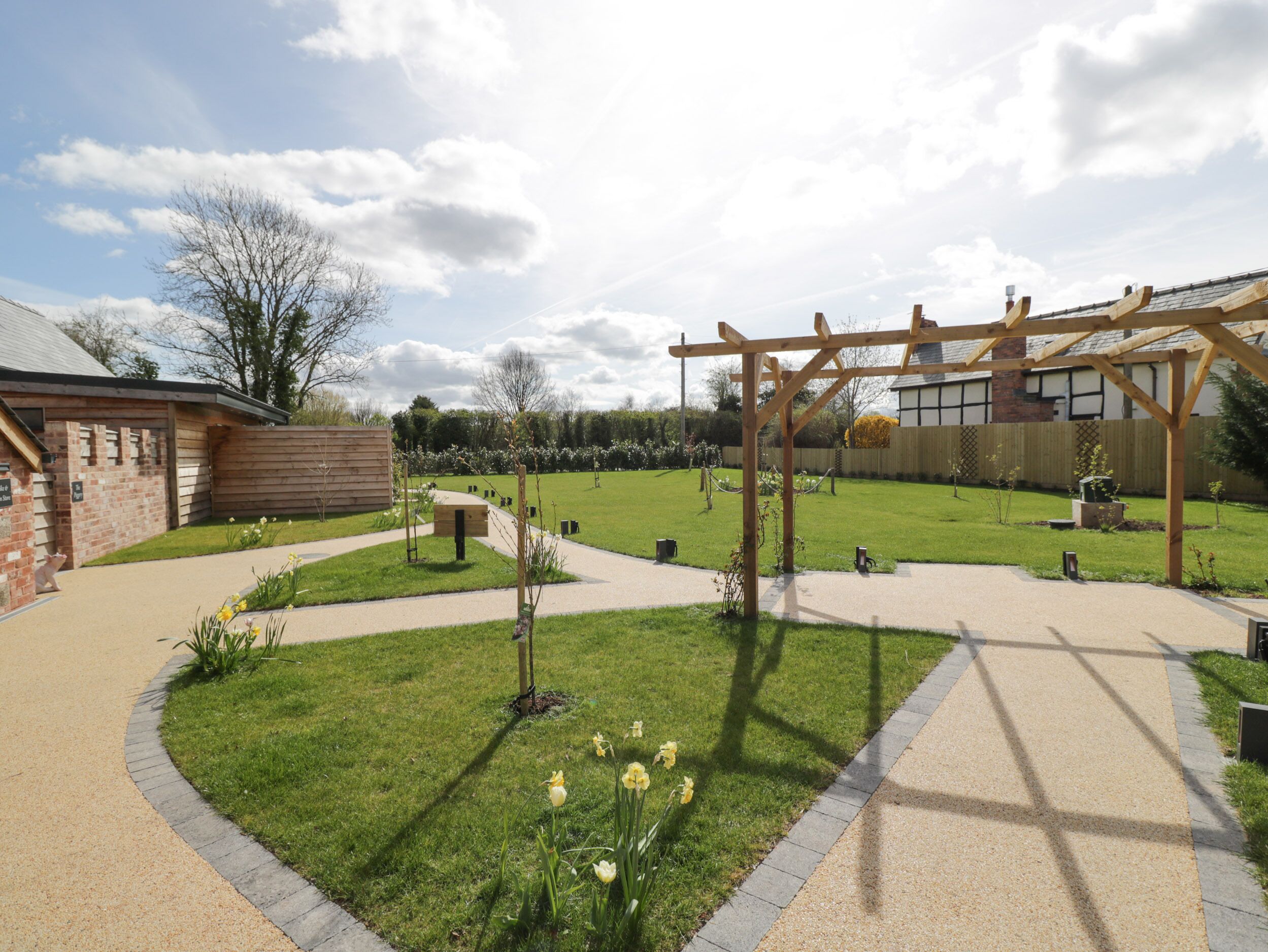 A well-maintained garden with a wooden pergola, a brick building, and a clear sky.