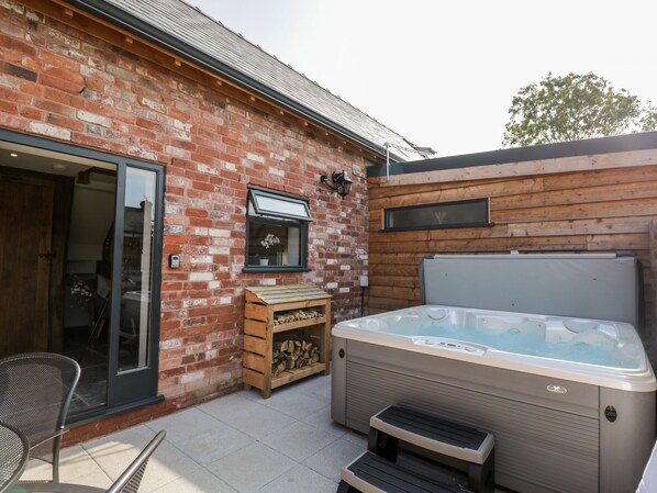 Un edificio de ladrillo con terraza de madera, jacuzzi y una silla.