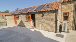 A stone building with a tiled roof, solar panels, and a small window. - Yeoman's Cottage (Pickering)