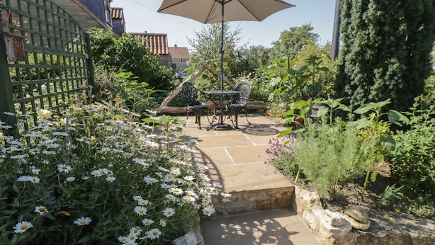 A garden patio with a table and chairs, surrounded by a variety of plants and flowers. - Yeoman's Cottage (Pickering)