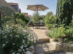 A garden patio with a table and chairs, surrounded by a variety of plants and flowers. - Yeoman's Cottage (Pickering)