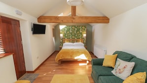 A cozy room with a bed, a green sofa, a wooden bench, and a TV on the wall. - Yeoman's Cottage (Pickering)