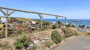Eine Küstenlandschaft mit Holzbauten, Picknicktischen und Blick aufs Meer.