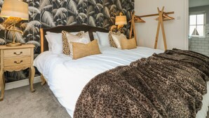 A bedroom with a bed, a nightstand, a lamp, a hanging lamp, a wooden easel, and a leopard print blanket. - Fistral Bay Cottage (Newquay)