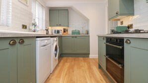 A compact kitchen with a washing machine, microwave, and oven. - Fistral Bay Cottage (Newquay)