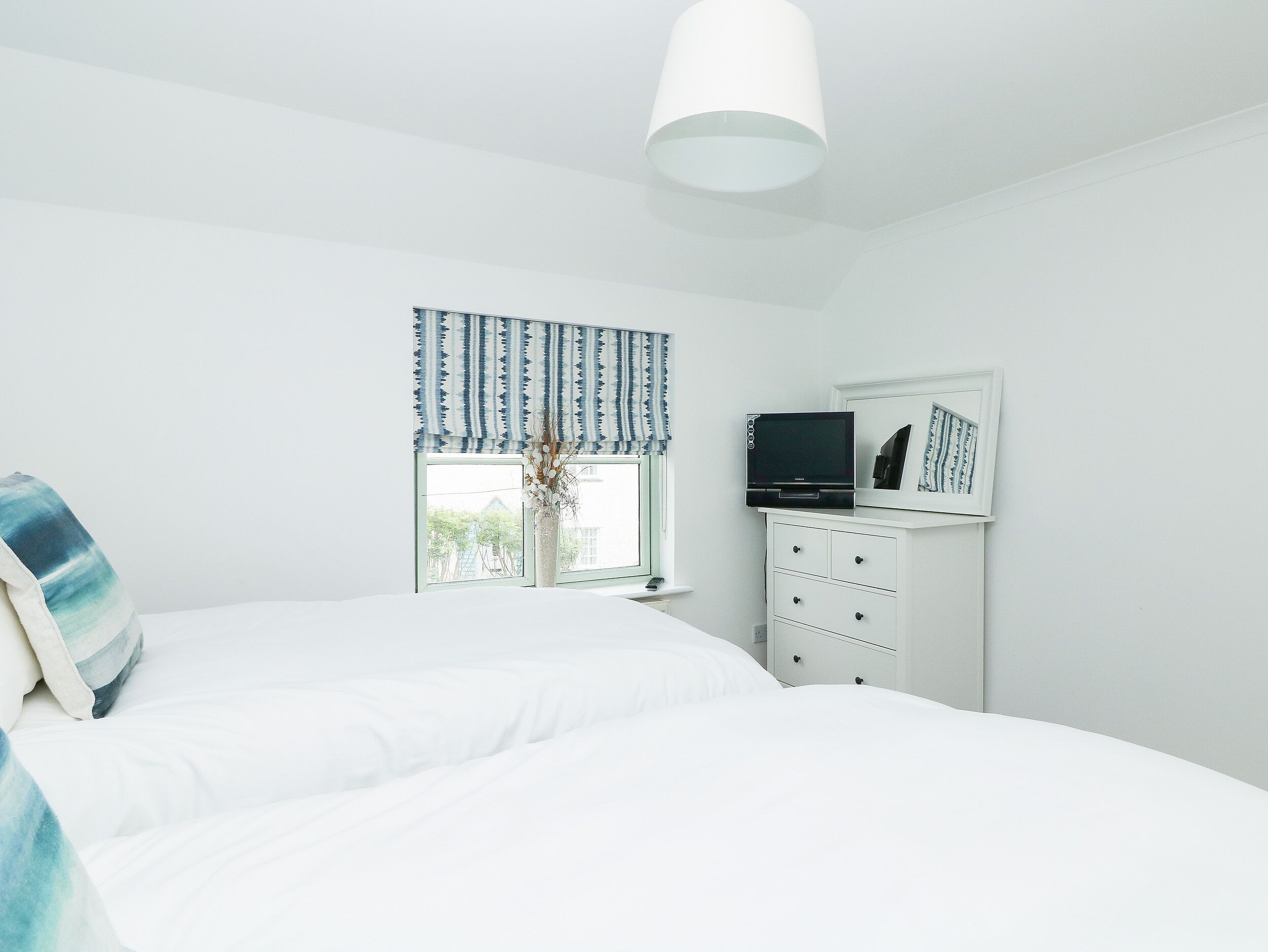 A bedroom with a bed, a dresser, a television, and a window with curtains.