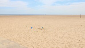 Une vaste plage de sable, parsemée de quelques objets et avec un navire visible au loin.