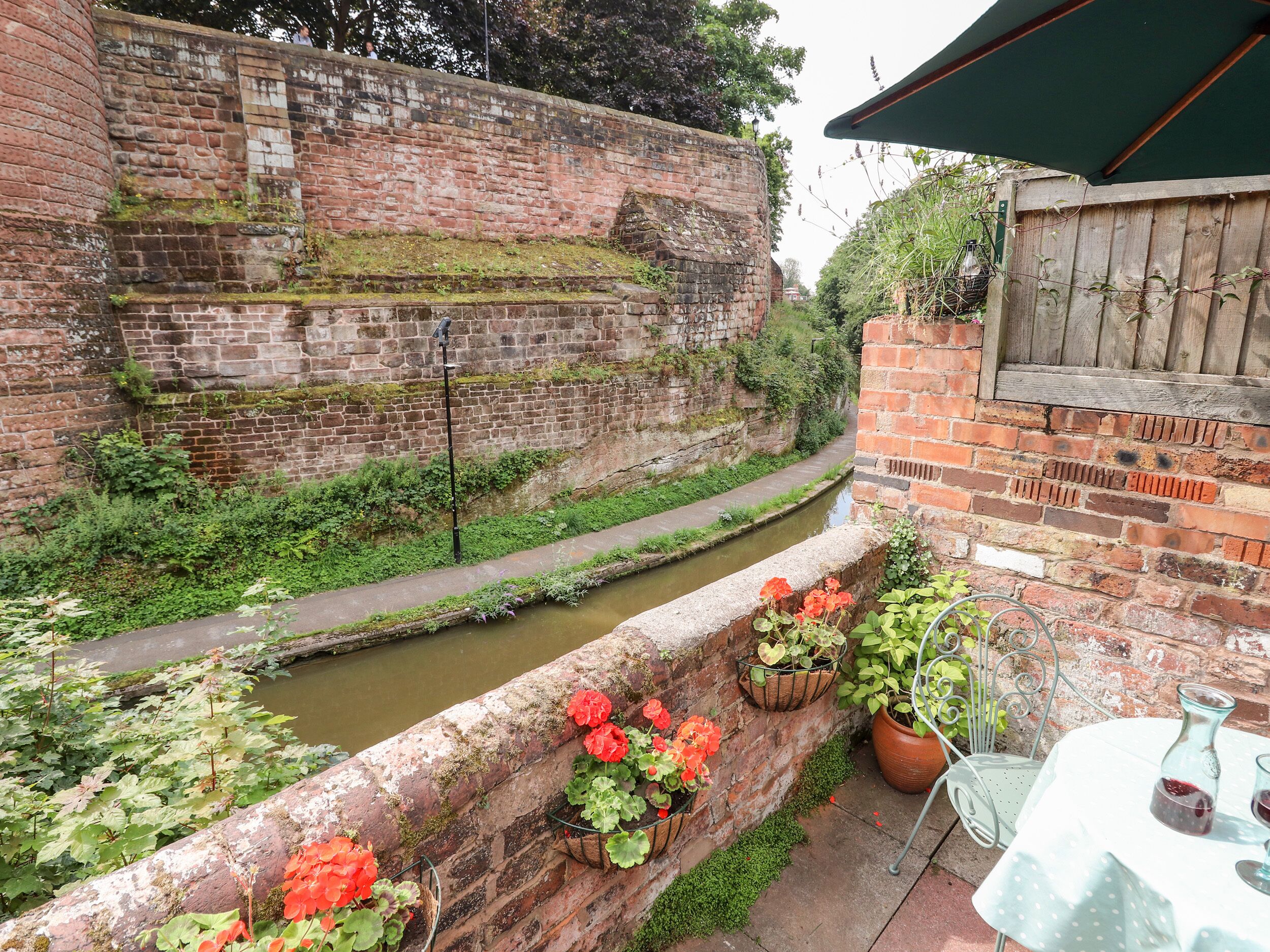 A brick wall with a narrow water channel, potted plants, and a table with glasses.