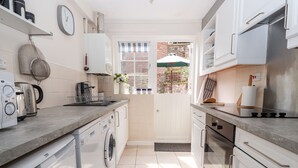 A modern kitchen with a washing machine, a kettle, and a stove. - Tower View Cottage (Chester)