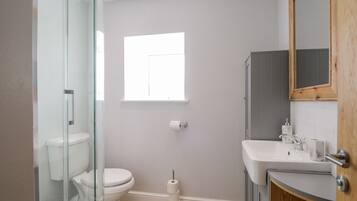 Een moderne badkamer met een douchecabine van glas, een toilet, een wastafel met houten kastje en een raam voor natuurlijk licht.