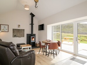 Ein modernes Wohnzimmer mit Kamin, Ledersofa, Holztisch und Blick auf einen Garten durch große Schiebeglasfenster.