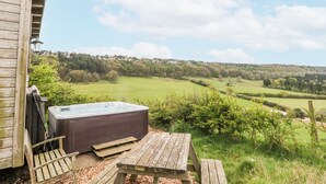 A wooden deck with a hot tub, a bench, and a view of a green landscape. - Shepherd's Hut (Scarborough)