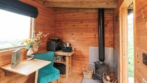 A cozy cabin interior with a wooden interior, a black wood stove, a table with a vase of flowers, and a view through the window. - Shepherd's Hut (Scarborough)