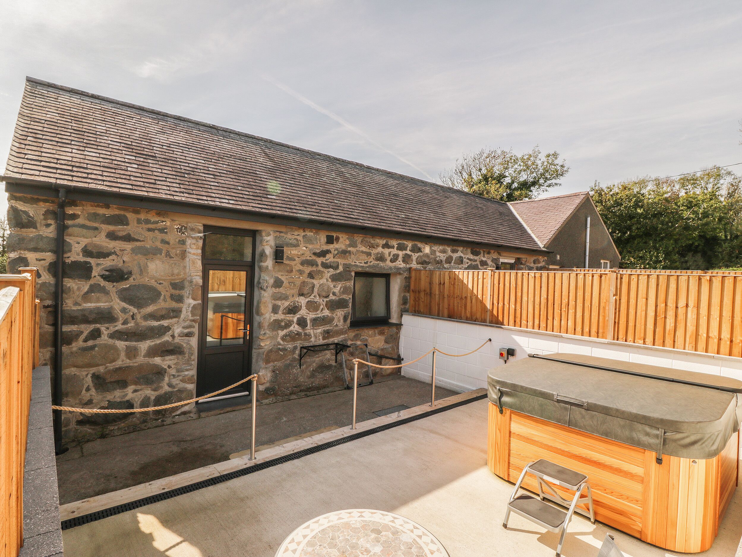 A stone building with a wooden door, a hot tub, and a wooden fence.