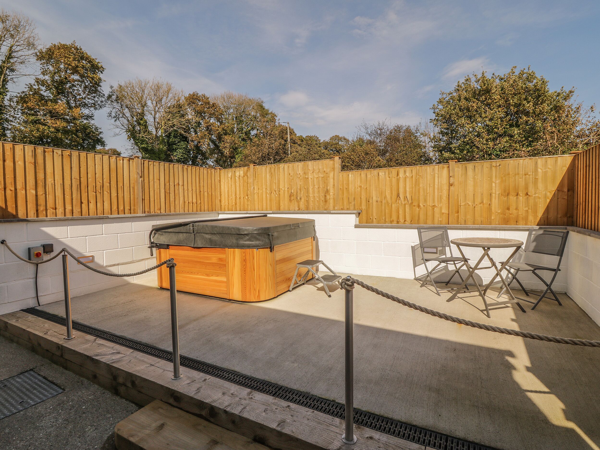 An outdoor hot tub area with a wooden deck, a seating area with chairs, and a wooden fence.