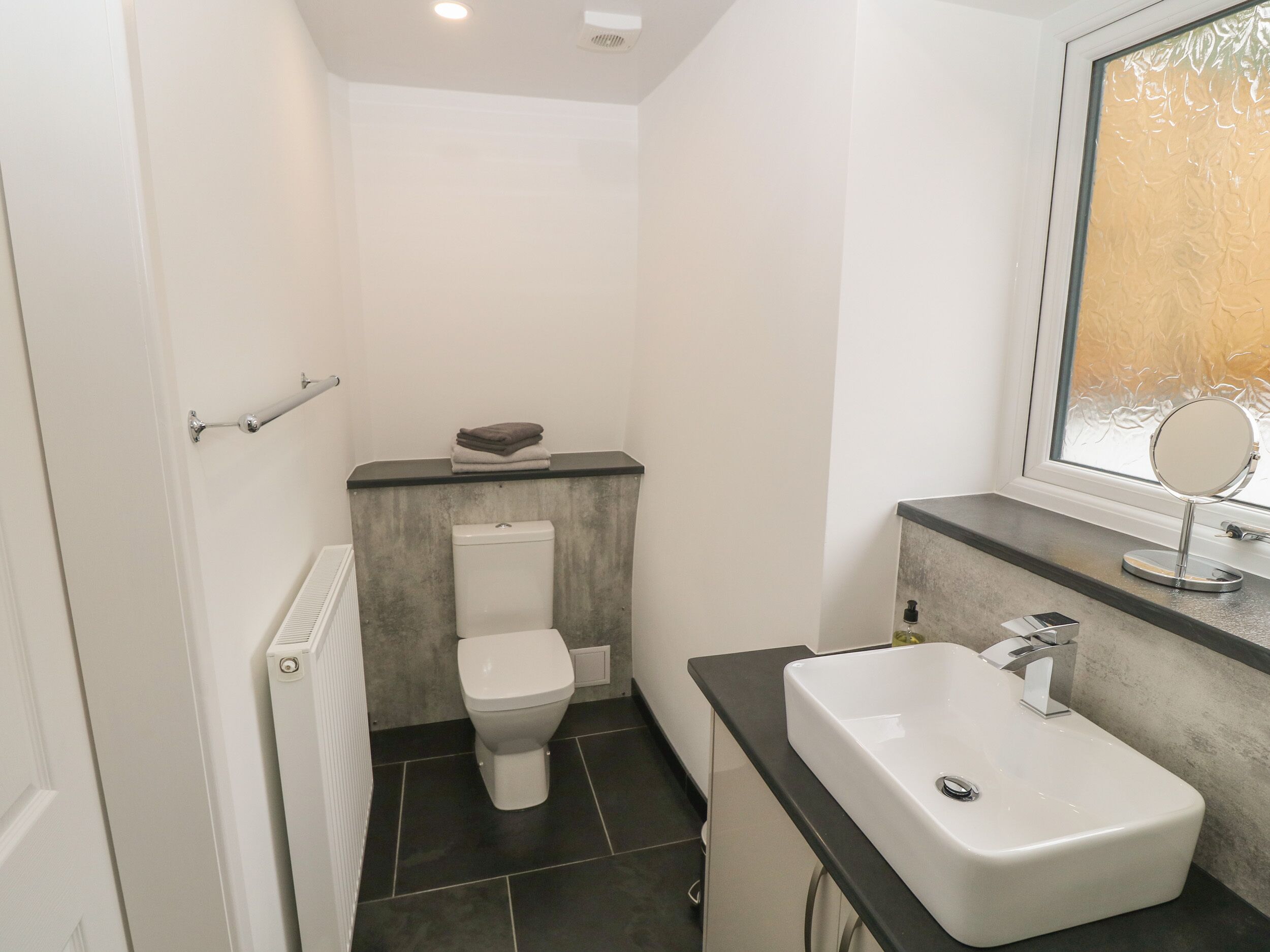 A compact bathroom with a toilet, a sink, and a window with frosted glass.