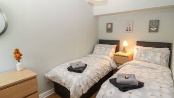 A bedroom with two beds, a bedside table with a lamp, a dresser, and wall art.