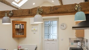 A kitchen with wooden beams, a white door, a clock, and a fruit bowl on the counter. - Glan Meon Cottage (Barmouth)
