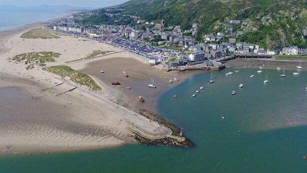 An aerial view of a coastal town with a beach, boats, and a mountainous backdrop. - Glan Meon Cottage (Barmouth)