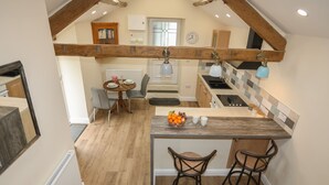 A kitchen with a wooden island, two bar stools, a dining table with chairs, and a view of the living area. - Glan Meon Cottage (Barmouth)
