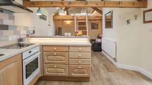 A kitchen with wooden beams, a central island, and a view to the living area. - Glan Meon Cottage (Barmouth)