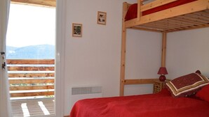 Ein Einzelzimmer mit Etagenbett, einer roten Tagesdecke, einem kleinen Nachttisch mit Lampe und einem Fenster mit Bergblick.