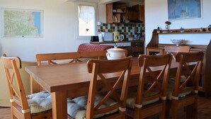 Ein Essbereich mit Holztisch und -stühlen, im Hintergrund eine Küche und eine Karte an der Wand.