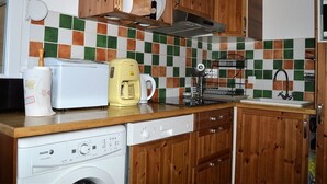 Eine kleine Küche mit Holzschränken, einer Waschmaschine, einer Kaffeemaschine und einem Toaster.