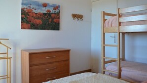 Ein Schlafzimmer mit einem Etagenbett, einer Holzkommode, einem Blumenbild und einer Holzleiter.