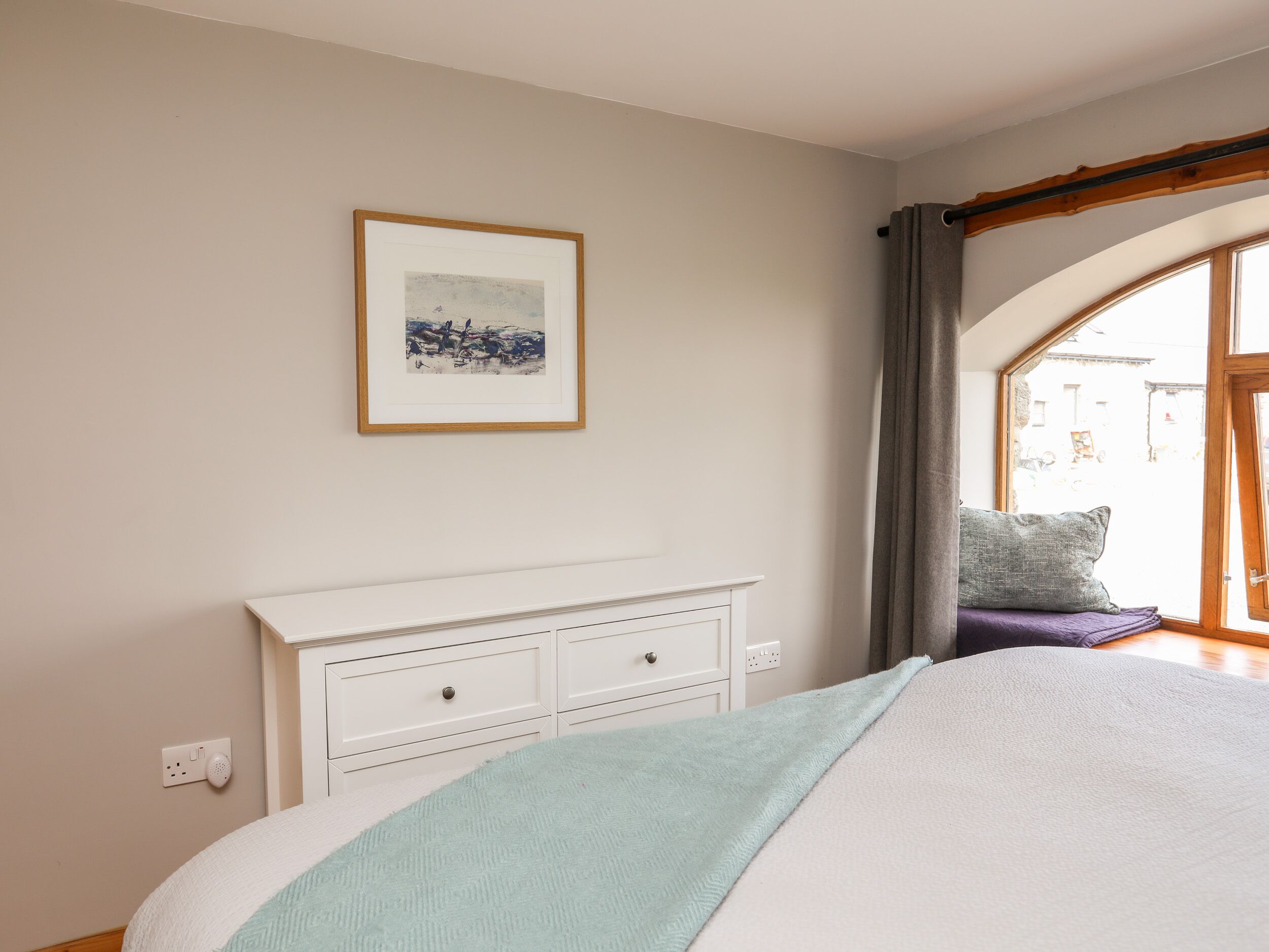 A bedroom with a bed, a white dresser, a framed picture on the wall, and a window with curtains.