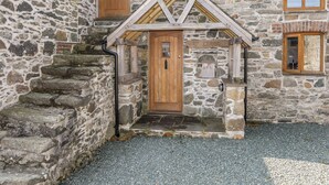 A stone building with a wooden door and a small porch. - Ty Cerrig (Gaerwen)