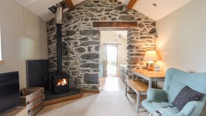 A cozy room with a stone wall, a fireplace, a blue armchair, and a small table with a lamp. - Ty Cerrig (Gaerwen)