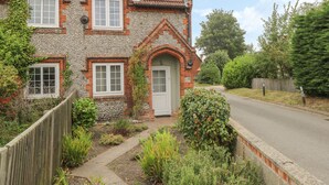 A two-story house with a stone facade, a tiled roof, and a wooden fence. - Compass Cottage (Holt)