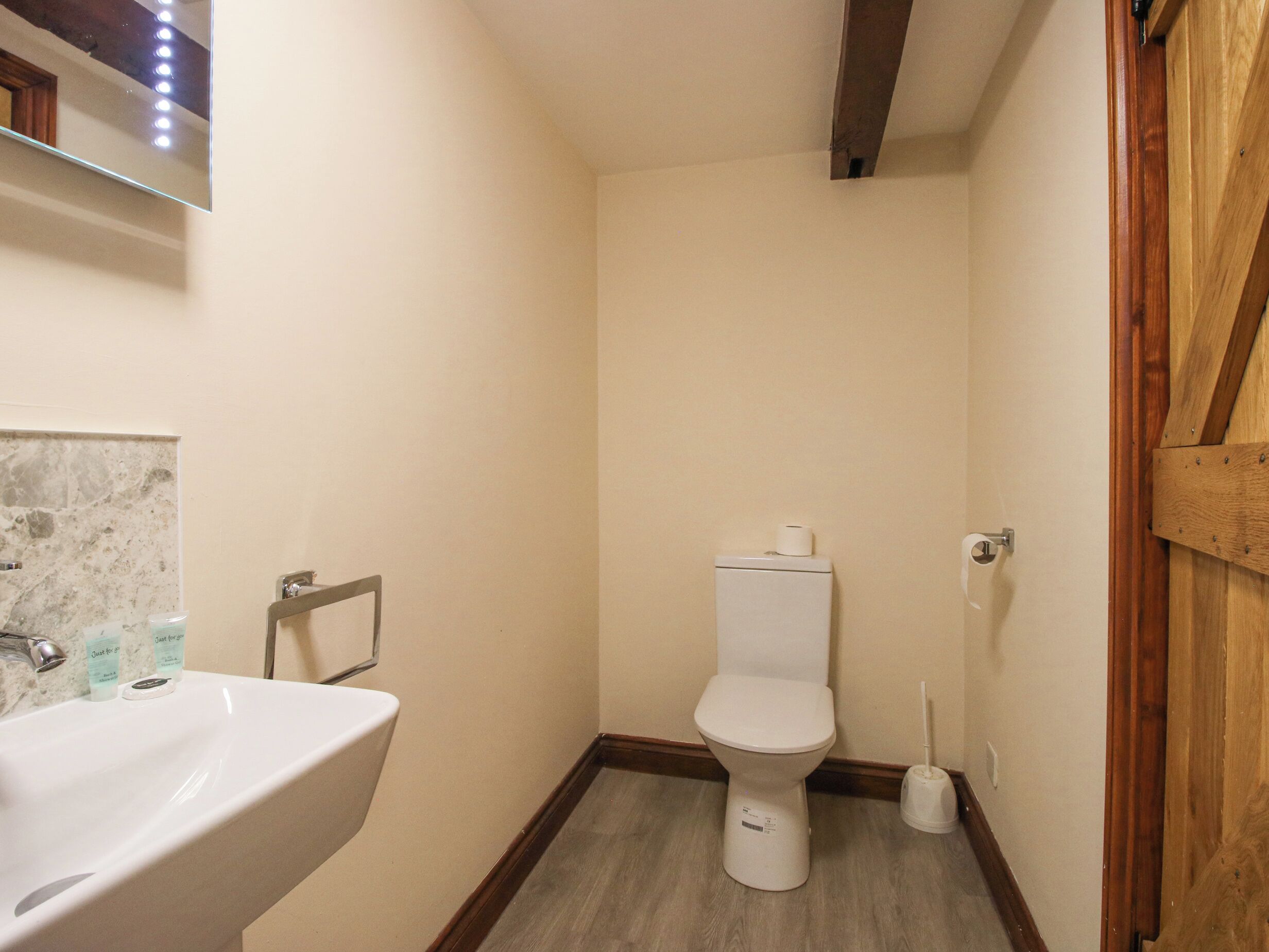 A small bathroom with a white sink, toilet, and a wooden floor.