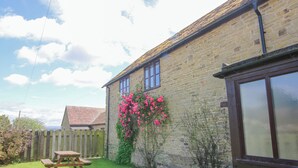 Ein Steinhaus mit Holzzaun, Picknicktisch und rosa Blumen.