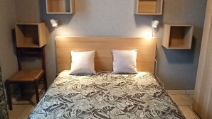 Ein Schlafzimmer mit einem Holzkopfteil, zwei Nachttischlampen, einer blumigen Bettdecke und fest installierten Regalen an den Wänden.