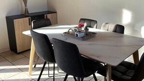 Ein moderner Essbereich mit einem Marmortisch, schwarzen Polsterstühlen, einer kleinen Kommode und einer dekorativen Vase mit Trockenpflanzen.