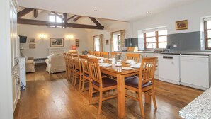 Uma sala de jantar ampla com cadeiras de madeira e uma mesa grande, uma cozinha com eletrodomésticos brancos e uma sala de estar acolhedora com um sofá e uma lareira.
