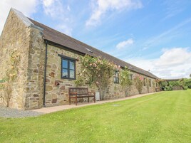 A stone building with a sloped roof, a bench, and a well-maintained lawn.