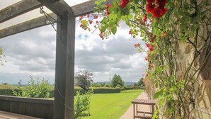 Eine hölzerne Pergola mit einer Bank, ein Weg, der zu einer Rasenfläche führt, und eine Aussicht auf die Landschaft.