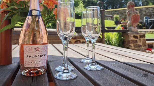 Una botella de prosecco y dos copas de vino vacías sobre una mesa de madera al aire libre.