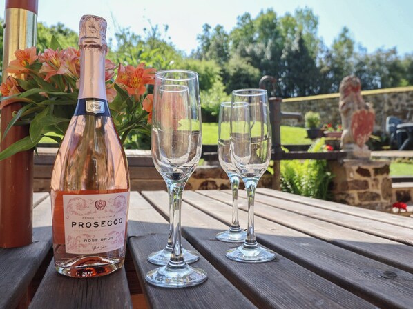Una botella de prosecco y dos copas de vino vacías sobre una mesa de madera al aire libre.