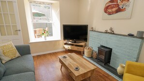 Una sala de estar con un sofá, una mesa de centro, un televisor, una chimenea y una ventana con persianas.