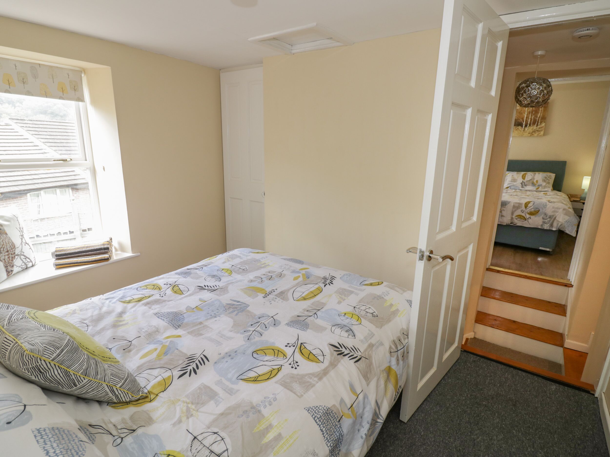 Un dormitorio con cama, ventana con persianas, puerta que da a otra habitación y una escalera.
