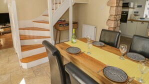 Un comedor con una mesa de madera preparada para dos personas, un pilar de piedra y una cocina al fondo.